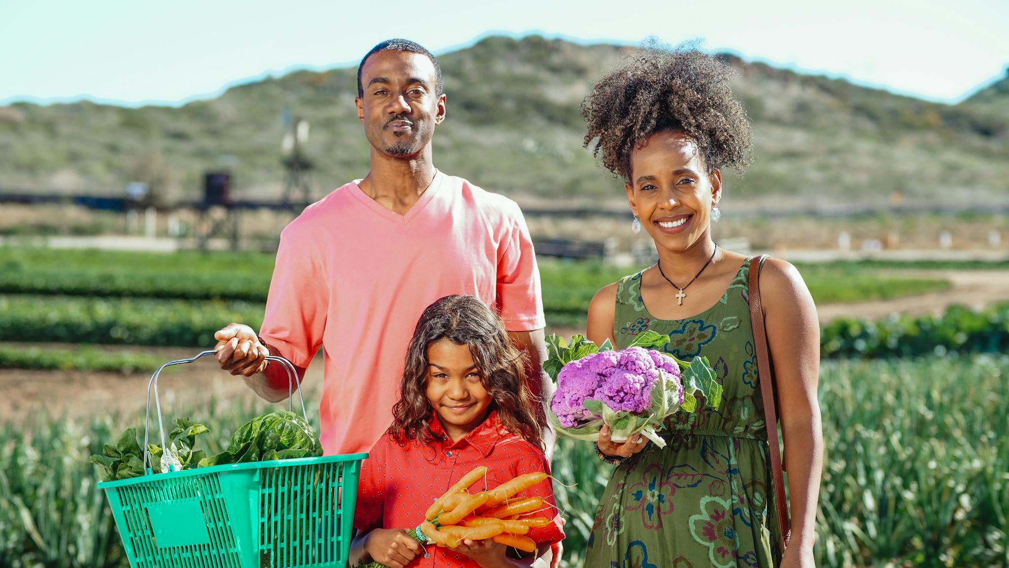 Smiling family posing with fresh vegetables in a lush farm setting.